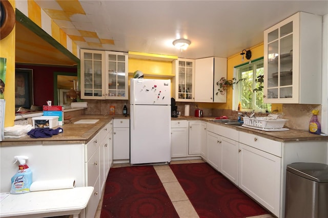 kitchen featuring sink, backsplash, white cabinets, dark tile patterned flooring, and white fridge