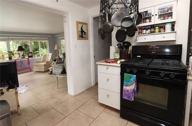 kitchen with black range with gas cooktop, light tile patterned floors, and white cabinetry