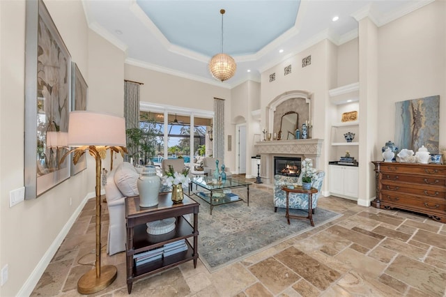 sitting room with stone tile floors, baseboards, a tray ceiling, a glass covered fireplace, and crown molding