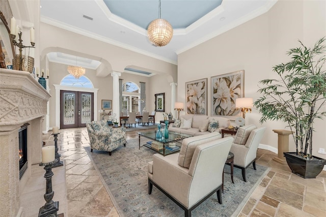 living room with decorative columns, a high ceiling, a tray ceiling, ornamental molding, and french doors