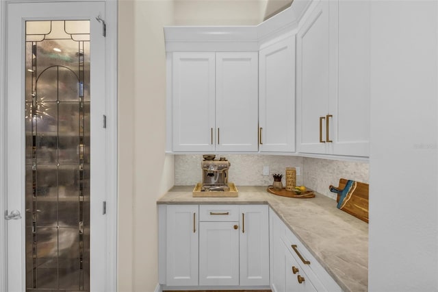 bar with backsplash, light stone counters, and white cabinets