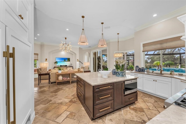 kitchen with pendant lighting, white cabinets, ornamental molding, a notable chandelier, and light stone countertops