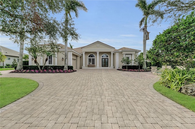 greek revival house featuring french doors, decorative driveway, an attached garage, and stucco siding