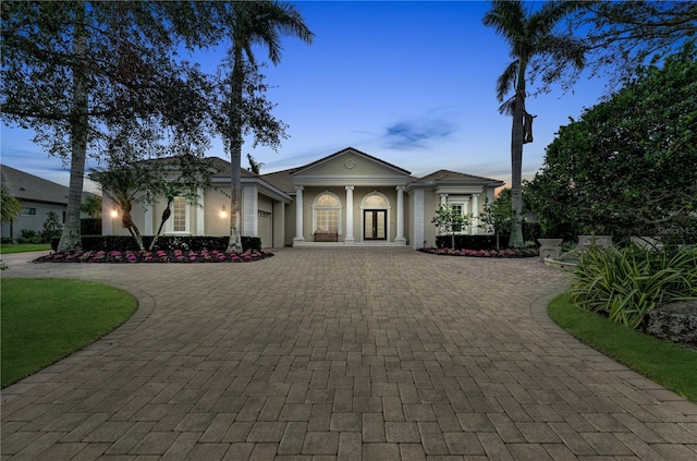 greek revival house with an attached garage, decorative driveway, and stucco siding