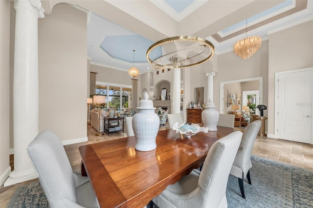 dining space with ornamental molding, a tray ceiling, stone tile floors, and ornate columns