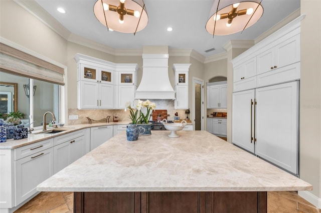 kitchen featuring glass insert cabinets, a center island, decorative light fixtures, premium range hood, and white cabinetry