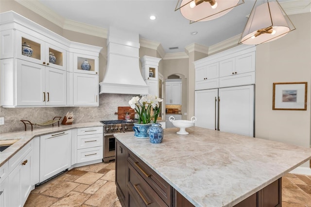 kitchen with high end appliances, pendant lighting, premium range hood, and stone tile floors