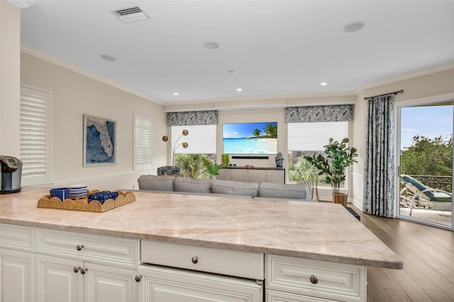 kitchen with wood finished floors, white cabinetry, open floor plan, ornamental molding, and light stone countertops