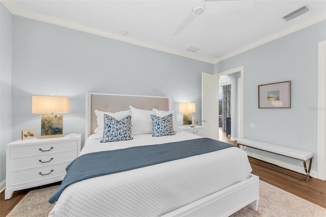 bedroom with baseboards, wood finished floors, visible vents, and crown molding