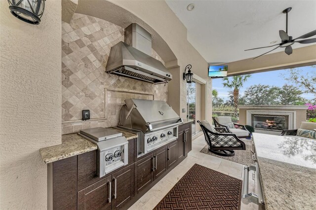 view of patio / terrace with exterior kitchen, a glass covered fireplace, ceiling fan, and area for grilling