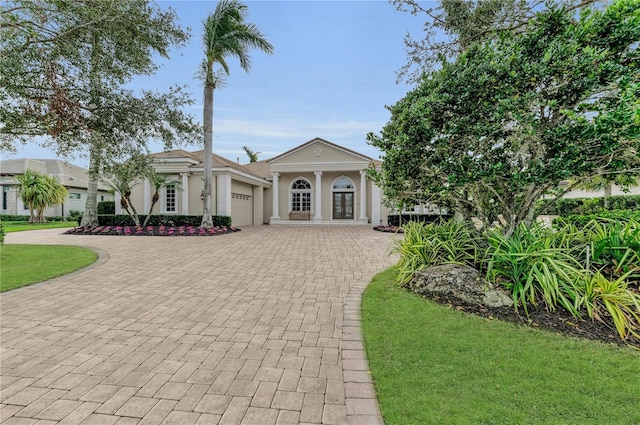 greek revival house with an attached garage, a front yard, decorative driveway, and stucco siding