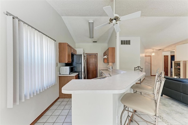 kitchen featuring a breakfast bar area, appliances with stainless steel finishes, a textured ceiling, light tile patterned flooring, and kitchen peninsula