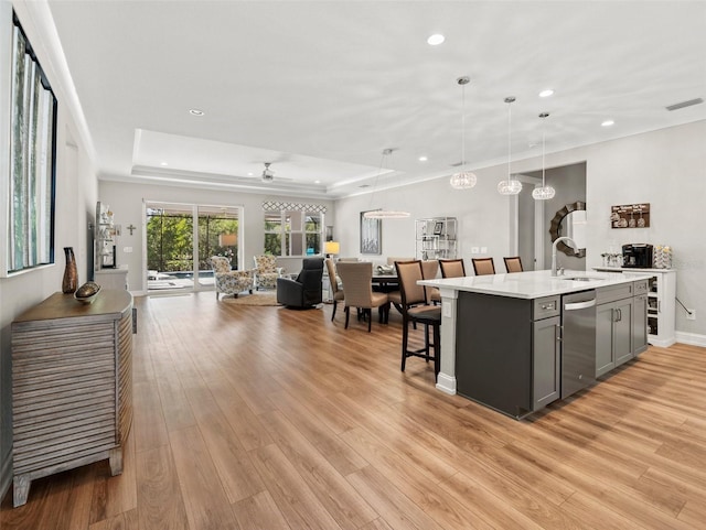 kitchen featuring dishwasher, pendant lighting, an island with sink, and a tray ceiling