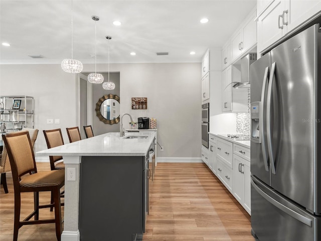 kitchen with a kitchen breakfast bar, an island with sink, pendant lighting, stainless steel appliances, and white cabinets