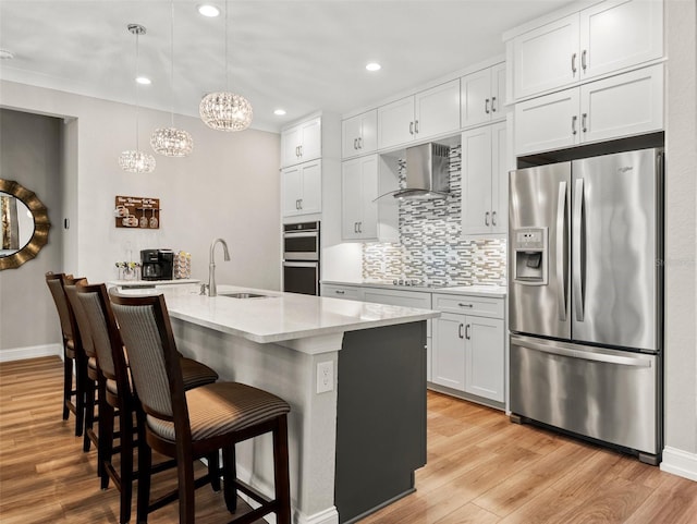 kitchen with white cabinetry, sink, a kitchen island with sink, stainless steel appliances, and wall chimney exhaust hood