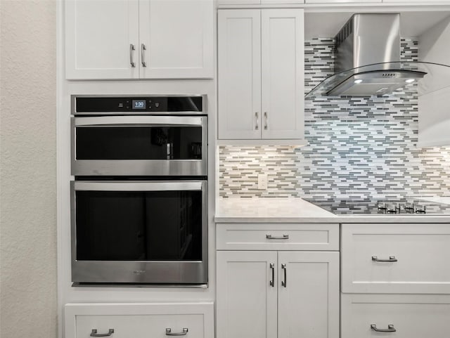 kitchen featuring white cabinetry, decorative backsplash, double oven, and wall chimney exhaust hood