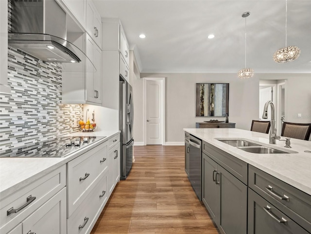 kitchen with pendant lighting, wall chimney range hood, sink, appliances with stainless steel finishes, and white cabinetry