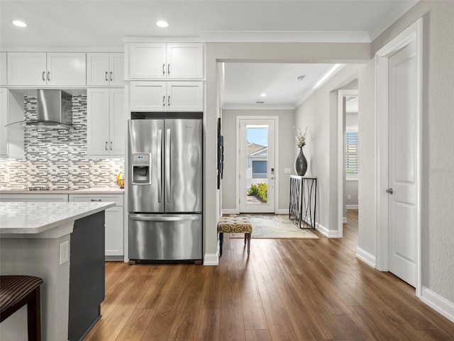 kitchen with crown molding, backsplash, white cabinets, stainless steel fridge with ice dispenser, and wall chimney exhaust hood