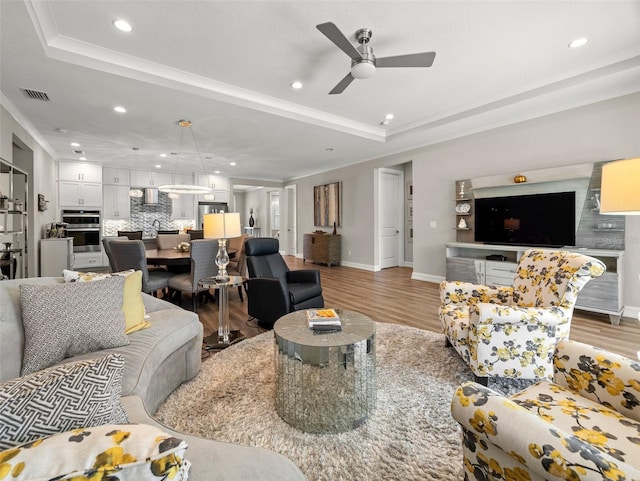 living room with crown molding, ceiling fan, a tray ceiling, and light hardwood / wood-style floors