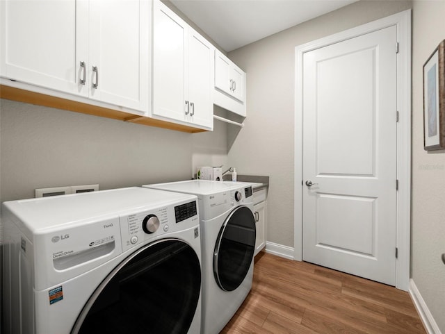 clothes washing area featuring washing machine and dryer, cabinets, and light wood-type flooring