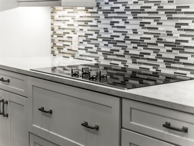 interior details with tasteful backsplash, black electric cooktop, and gray cabinetry