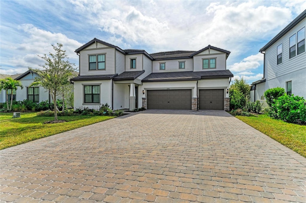 view of front facade with stone siding, a front lawn, decorative driveway, and an attached garage