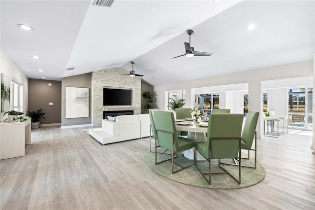 dining area with ceiling fan, a stone fireplace, lofted ceiling, and light hardwood / wood-style floors