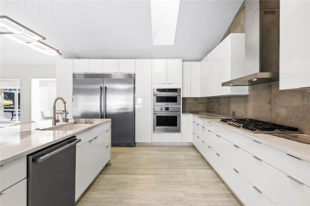 kitchen with sink, white cabinets, backsplash, stainless steel appliances, and wall chimney range hood