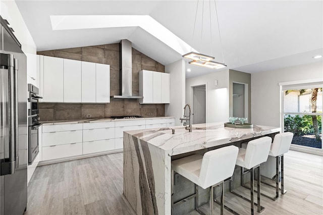 kitchen featuring sink, white cabinets, hanging light fixtures, a kitchen island with sink, and wall chimney exhaust hood