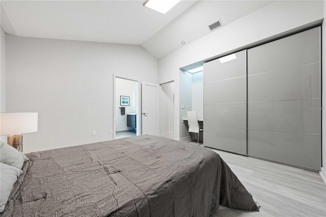 bedroom with ensuite bath, vaulted ceiling, and light wood-type flooring