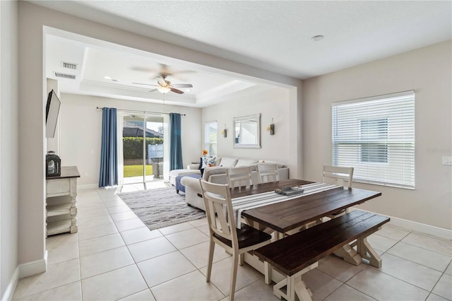 tiled dining space featuring ceiling fan and a tray ceiling