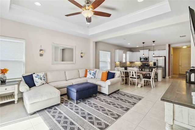 tiled living room with a raised ceiling and ceiling fan