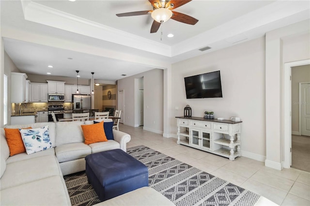 tiled living room with ceiling fan, a tray ceiling, and sink