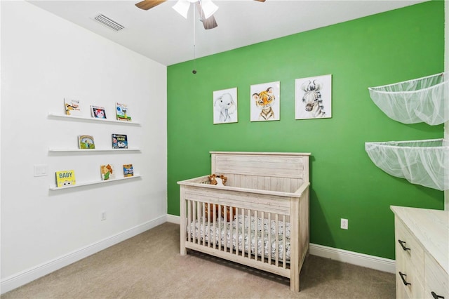 carpeted bedroom with a crib and ceiling fan