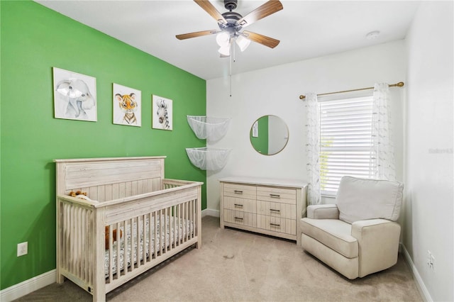 bedroom featuring a nursery area, light carpet, and ceiling fan