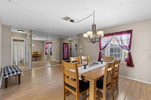 dining area featuring a chandelier, light hardwood / wood-style flooring, and a textured ceiling