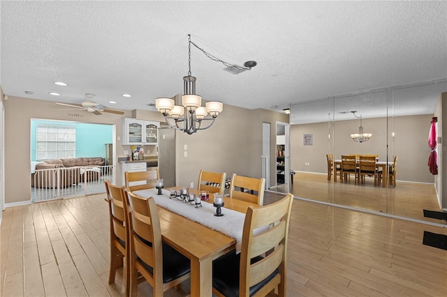 dining area with ceiling fan with notable chandelier, a textured ceiling, and light wood-type flooring