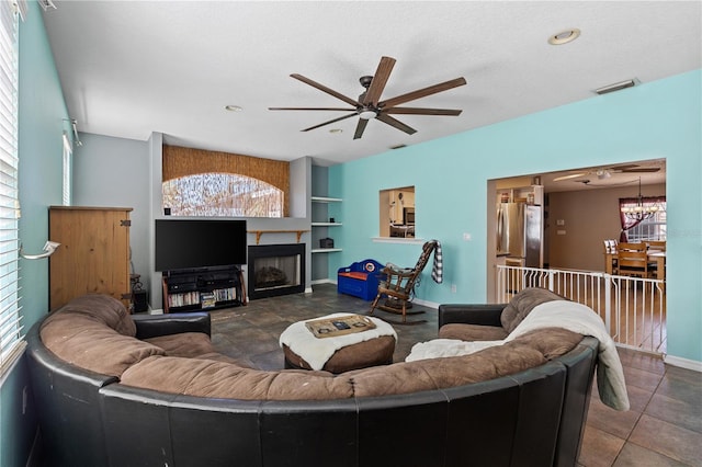 living room with ceiling fan with notable chandelier, built in features, and a textured ceiling