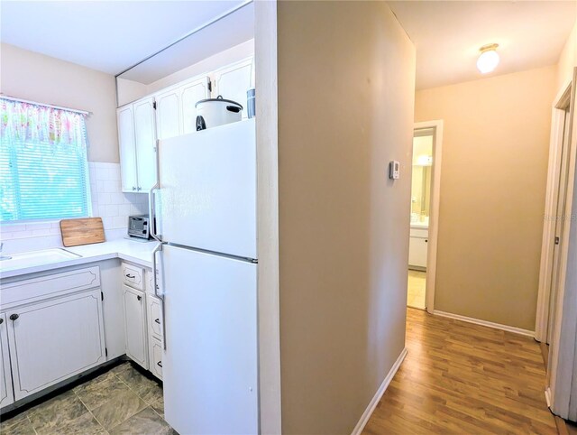 kitchen featuring baseboards, freestanding refrigerator, light countertops, white cabinetry, and backsplash