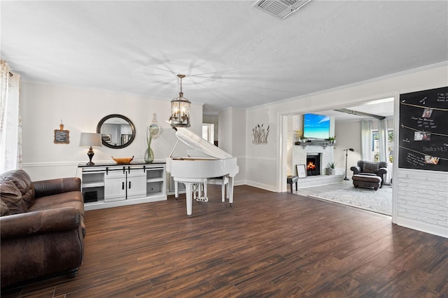 living room featuring dark wood-type flooring, an inviting chandelier, crown molding, a textured ceiling, and a fireplace