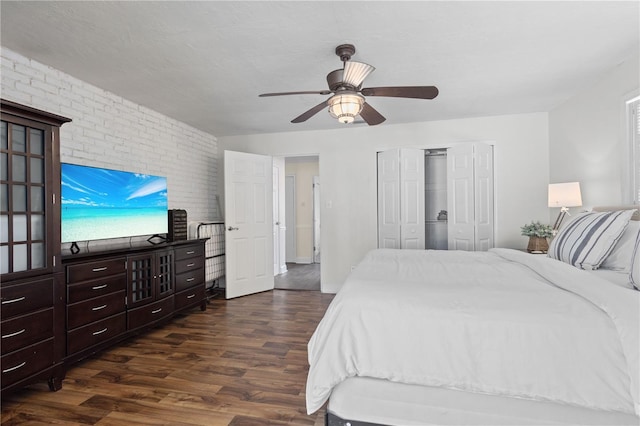 bedroom with a closet, dark hardwood / wood-style floors, ceiling fan, and brick wall