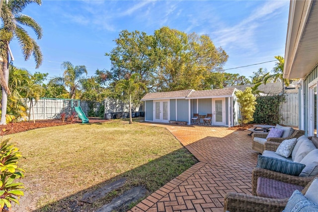 view of yard featuring french doors, an outdoor structure, a playground, and a patio area