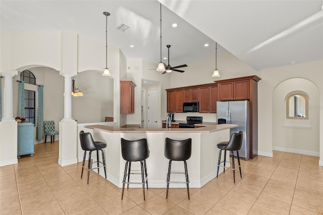 kitchen with light tile patterned floors, a kitchen breakfast bar, ceiling fan, decorative columns, and black appliances