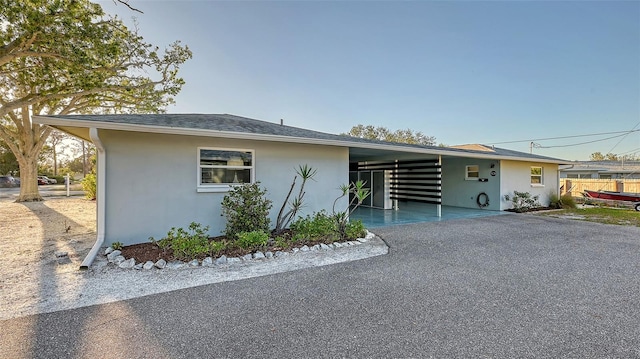 view of front of home with a carport, aphalt driveway, fence, and stucco siding