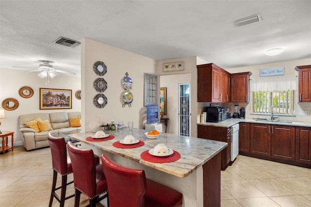 kitchen with dishwasher, sink, a kitchen bar, light tile patterned floors, and kitchen peninsula