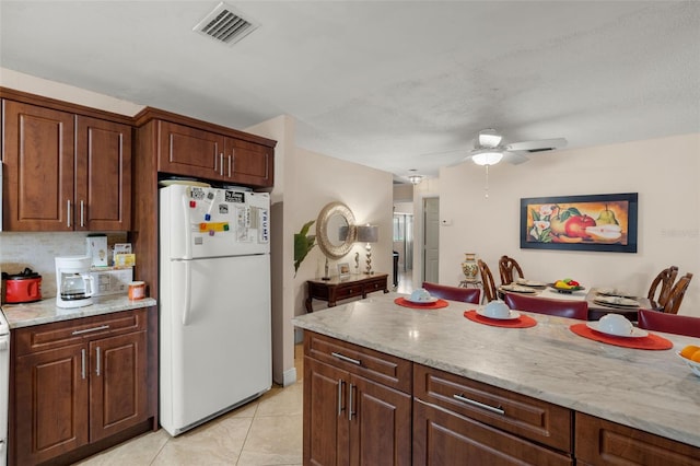 kitchen with light tile patterned flooring, light stone countertops, ceiling fan, and white refrigerator