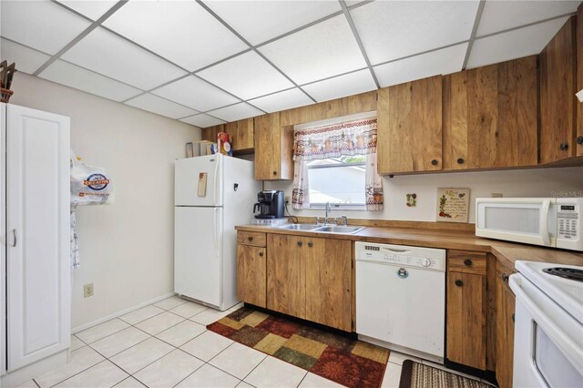 kitchen with a drop ceiling, sink, white appliances, and light tile patterned floors