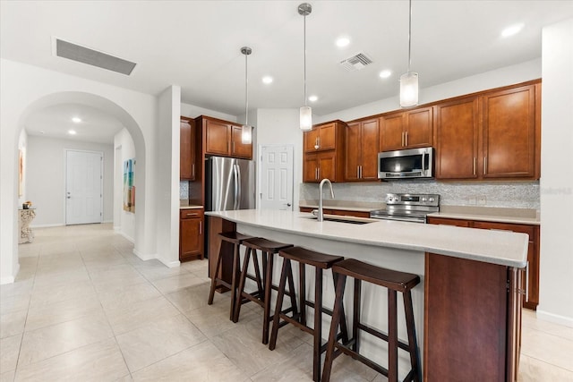 kitchen featuring hanging light fixtures, appliances with stainless steel finishes, sink, and a center island with sink