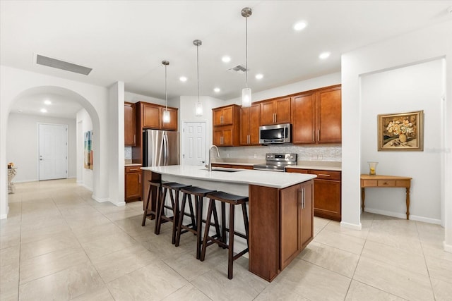 kitchen with sink, a breakfast bar area, appliances with stainless steel finishes, pendant lighting, and a kitchen island with sink