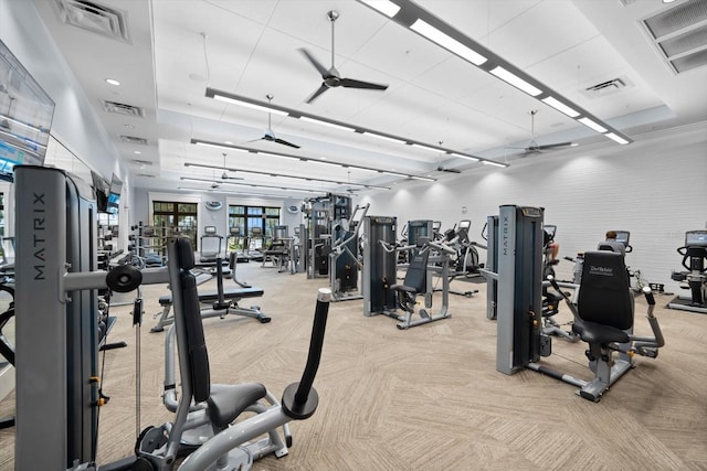 exercise room featuring a raised ceiling, light colored carpet, and ceiling fan